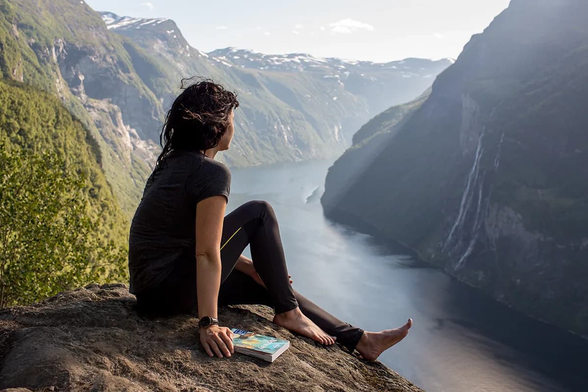 Una ragazza si rilassa su una roccia, godendo del panorama spettacolare di un fiordo norvegese, vivendo un’esperienza unica durante l’anno all’estero in Norvegia.