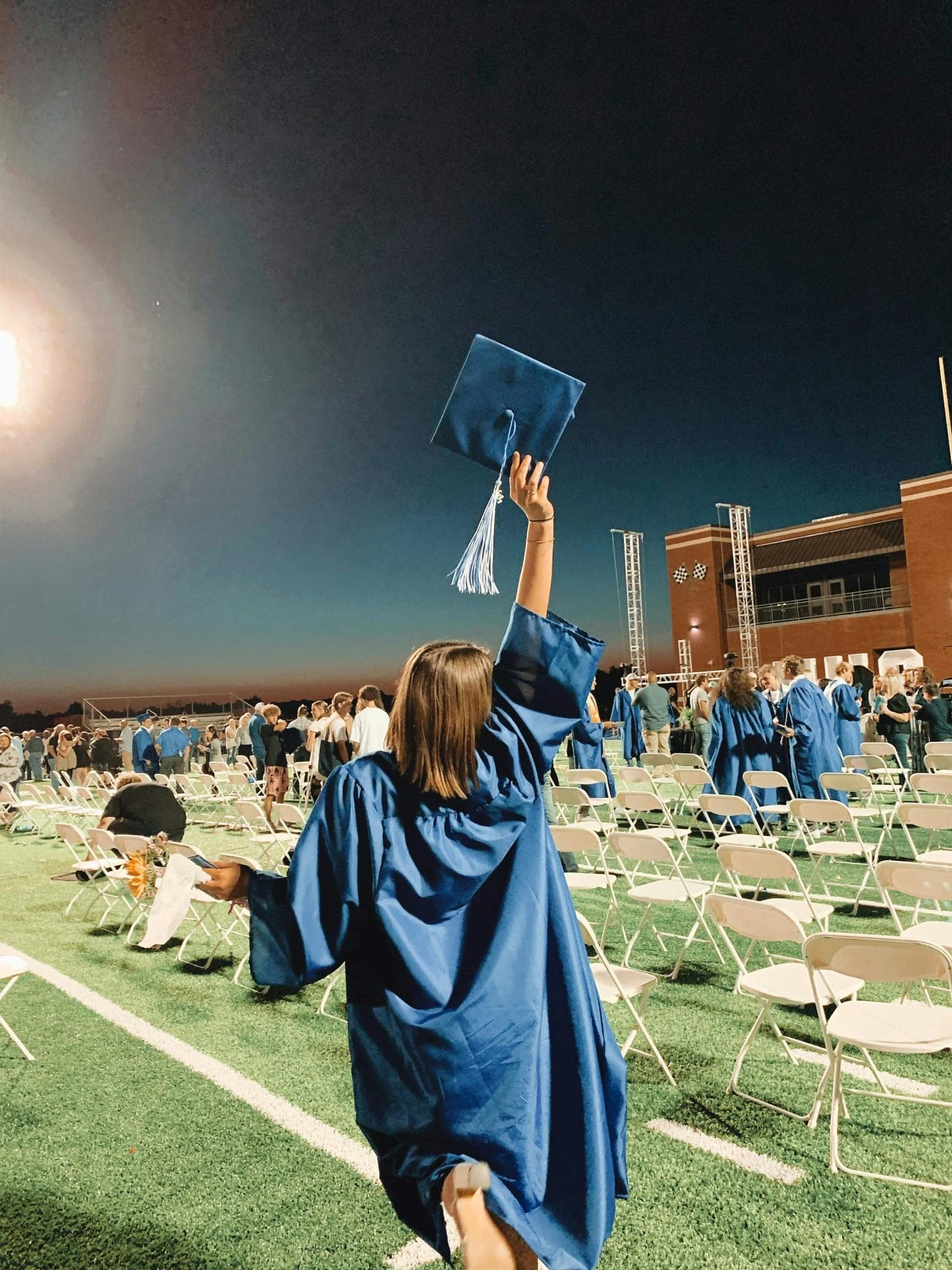Immagine di una studentessa che festeggia la laurea alzando il cappello sul campo da gioco, durante una cerimonia di graduazione negli Stati Uniti, tipica dell'anno all'estero negli USA.