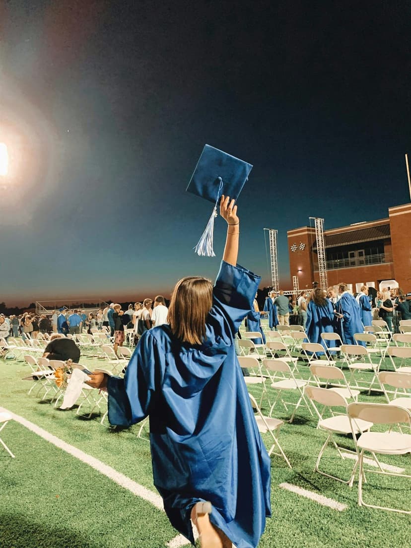 Immagine di una studentessa che festeggia la laurea alzando il cappello sul campo da gioco, durante una cerimonia di graduazione negli Stati Uniti, tipica dell'anno all'estero negli USA.