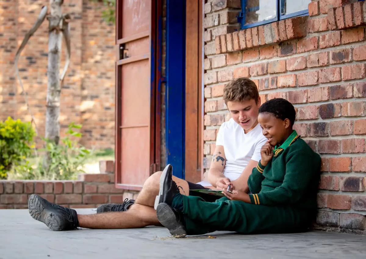 Studente internazionale e compagno sudafricano condividono un momento di apprendimento insieme, seduti all'aperto durante l'anno scolastico in Sudafrica.