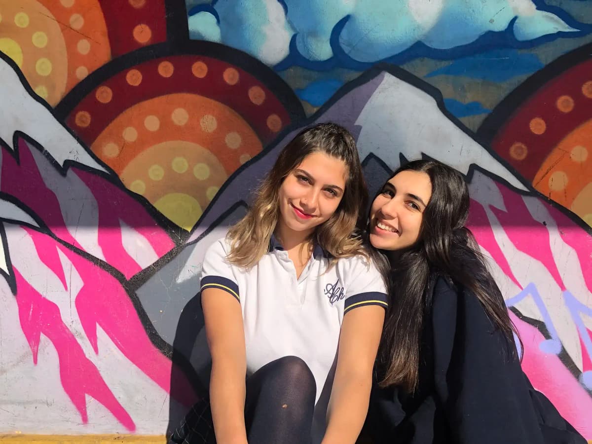 Due studentesse sorridono davanti a un murales colorato in Cile, vivendo un anno all’estero tra scuola, amicizie e scoperta culturale.