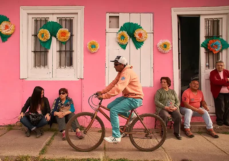 Scena di vita quotidiana in Cile con abitanti seduti davanti a una casa colorata e un uomo in bicicletta, simbolo di un anno all’estero in Cile.