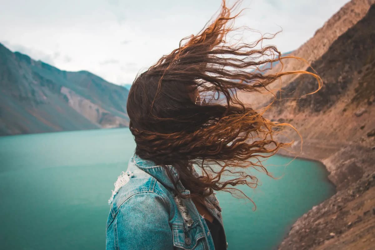 Studentessa con i capelli mossi dal vento davanti a un lago di montagna in Cile, durante un anno all’estero immerso nella natura.