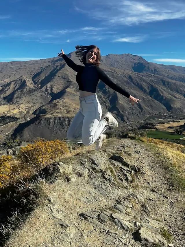 Studentessa salta in un paesaggio naturale durante un anno all’estero Nuova Zelanda, vivendo un’esperienza di scoperta e contatto con la natura.
